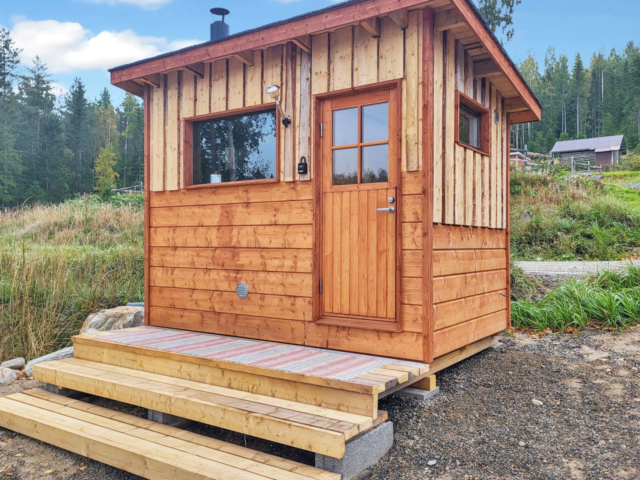 En liten stuga av trä med en ytterdörr, fönster och en ramp som leder fram till ingången.