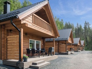A wooden cabin with a porch, outdoor seating, and a gravel driveway.
