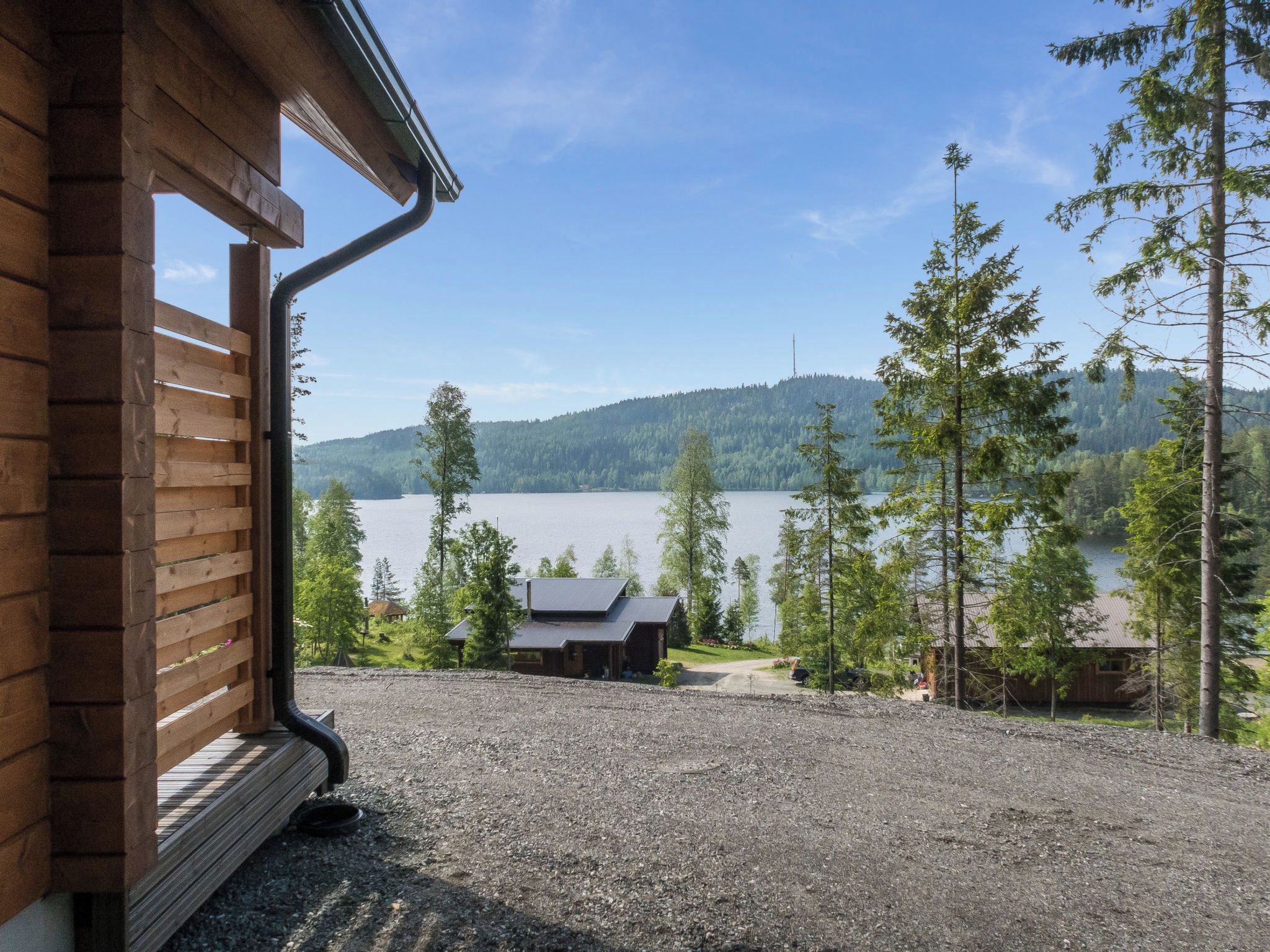 A wooden cabin with a gravel driveway leading to a lake view.