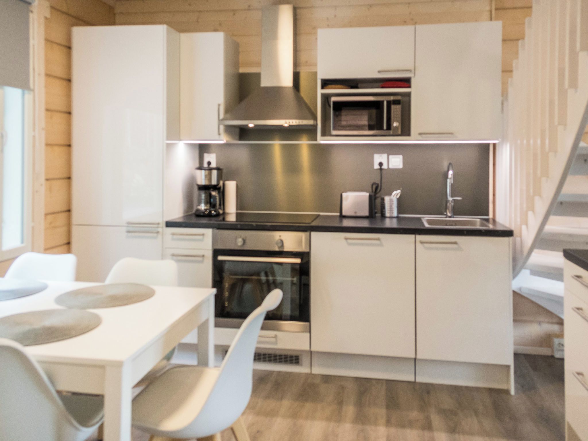A modern kitchen with white cabinetry, a stainless steel range hood, a built-in microwave, and a dining area with a white table and chairs.