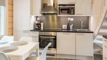 A modern kitchen with white cabinetry, a stainless steel range hood, a built-in microwave, and a dining area with a white table and chairs.