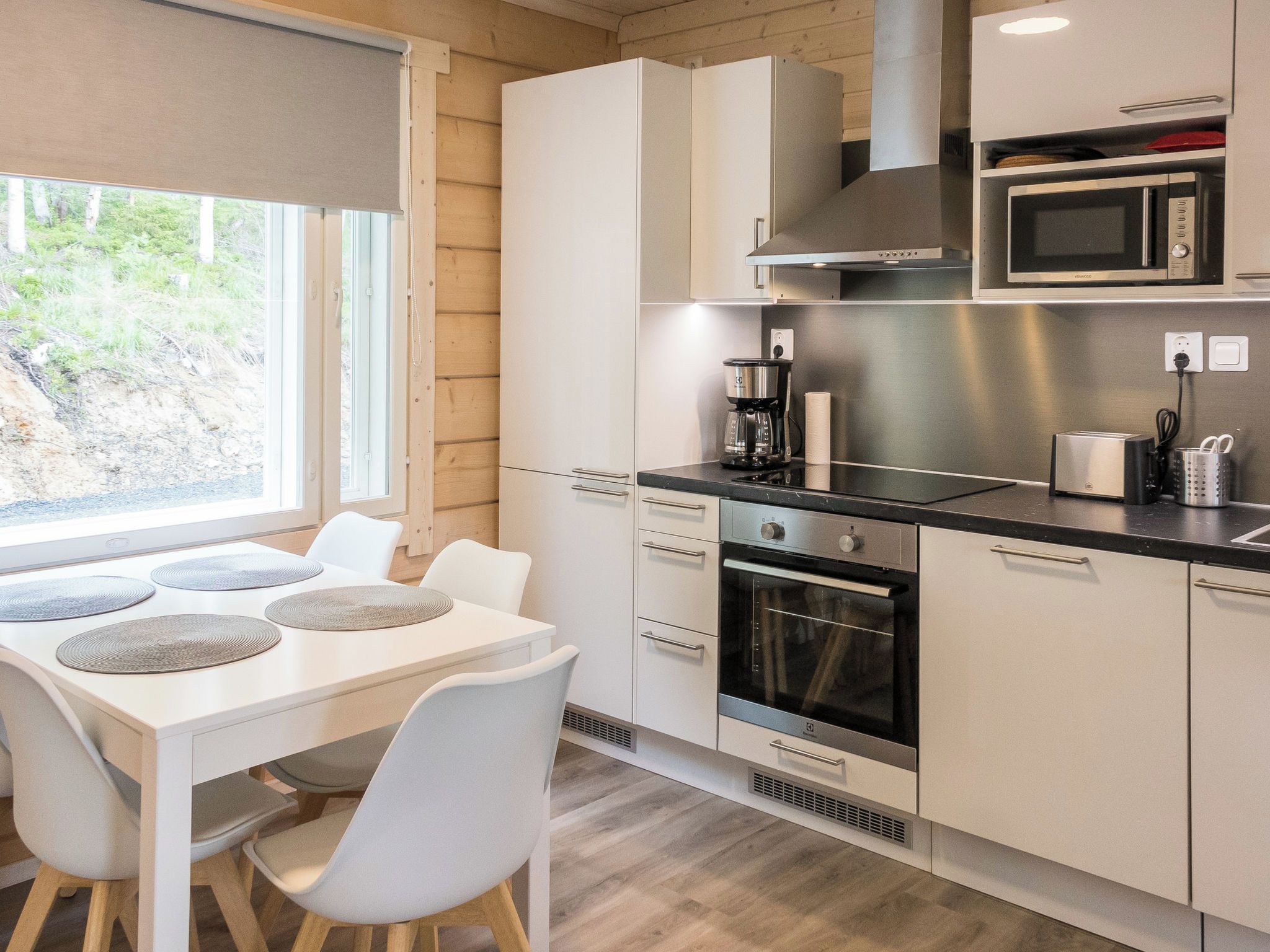 A modern kitchen with white cabinetry, a built-in microwave, a stove, and a window overlooking greenery.