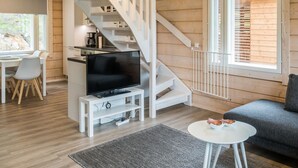 Un intérieur moderne avec un escalier en bois, un coin repas, un salon avec un canapé et un téléviseur posé sur un meuble blanc.