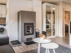 Un salon moderne avec une cheminée, un coin repas avec une table blanche et une cuisine visible à travers une porte ouverte.