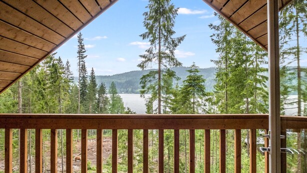 Ein Holzbalkon mit Tisch, mit Blick auf einen Wald und ein See.