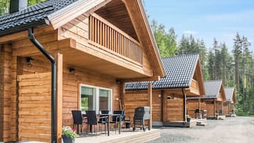 A wooden cabin with a porch, outdoor seating, and a gravel driveway.