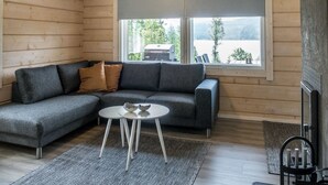Una sala de estar acogedora con un sofá seccional gris, una mesita blanca y un amplio ventanal con vistas al exterior.