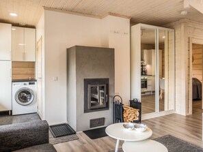 A modern living room with a fireplace, a dining area, and a kitchen visible through an open door.