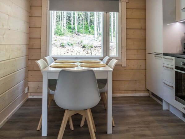 A compact kitchen with a dining table and chairs, a window with a view of trees, and a built-in oven.