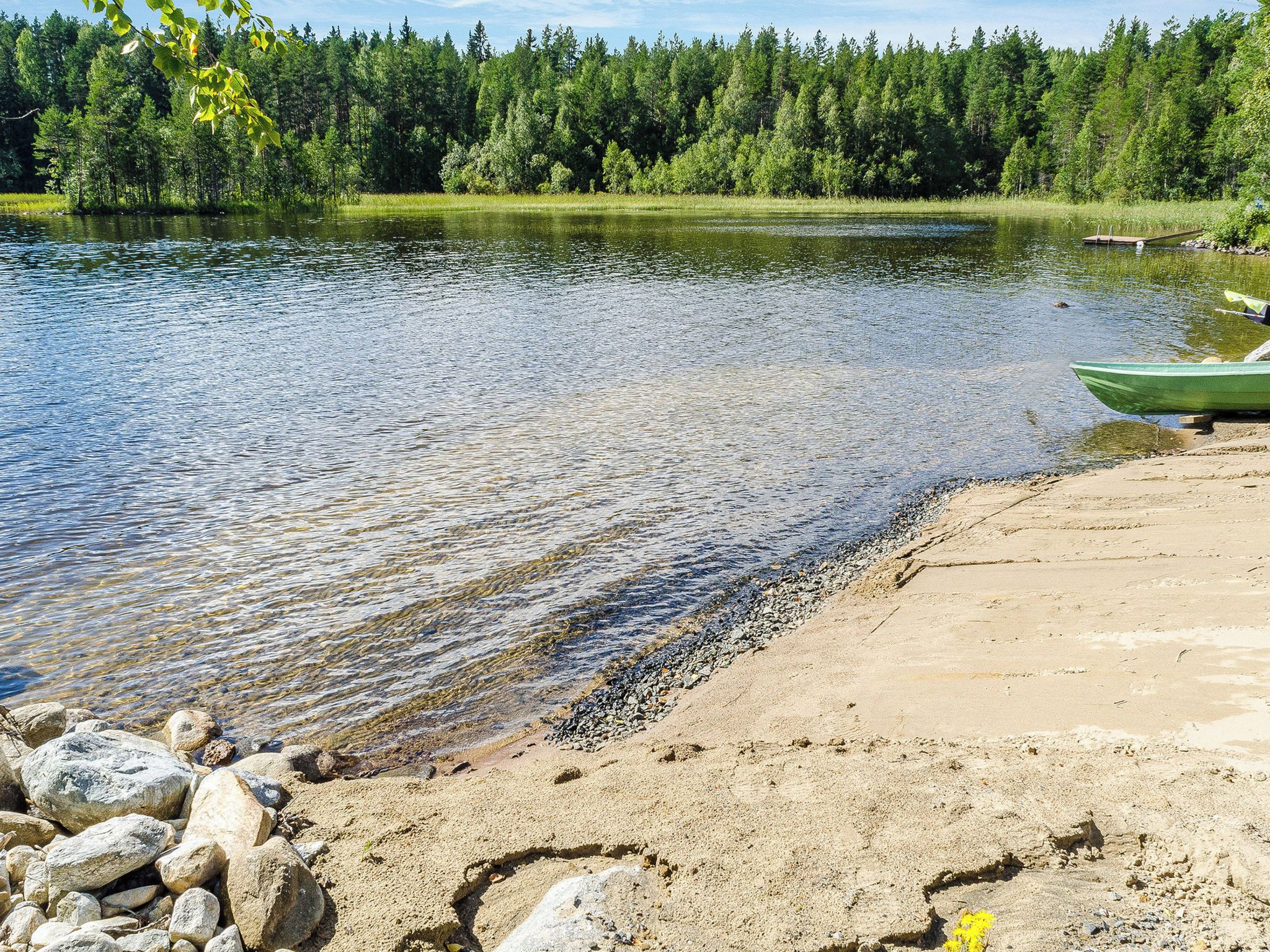 A calm lake with a sandy shore, surrounded by dense forest.