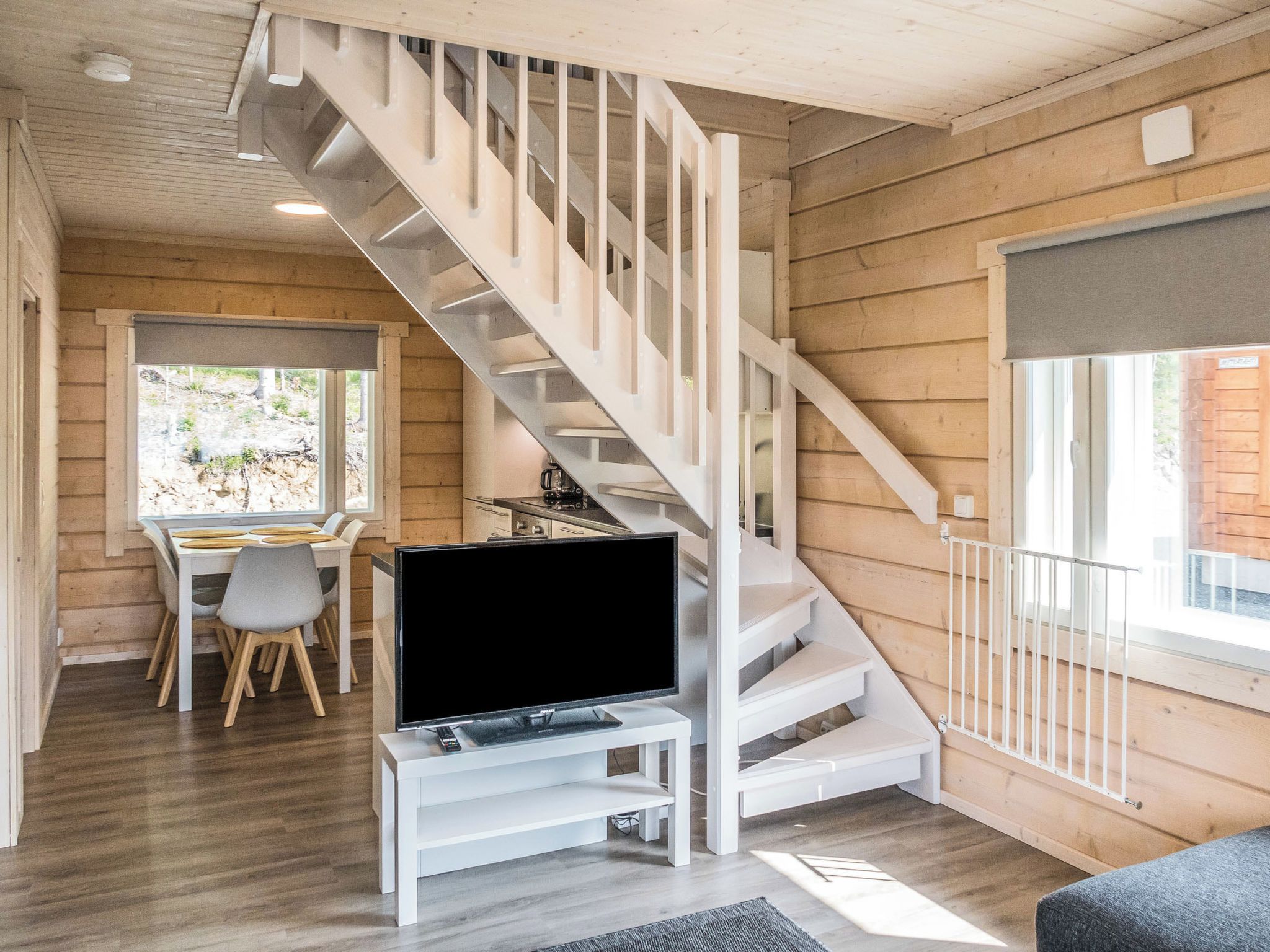 Un interno moderno con una scala in legno, una zona pranzo e un televisore su un mobile bianco.