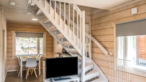 Un interior moderno con una escalera de madera, una zona de comedor con mesa y sillas, y un televisor de pantalla plana sobre un soporte blanco.