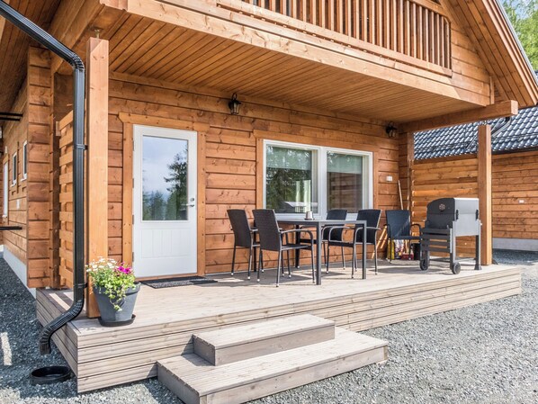 Une cabane en bois dotée d’un patio couvert, d’une table à manger avec des chaises et d’un barbecue.