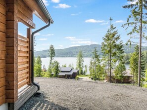 A wooden building with a gravel driveway leading to a lake with trees and a small cabin in the distance.