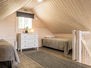 Ein gemütliches Schlafzimmer im Dachgeschoss mit Holzbalkendecke, einer weißen Kommode, zwei Betten und einem Fenster mit einer Pflanze.