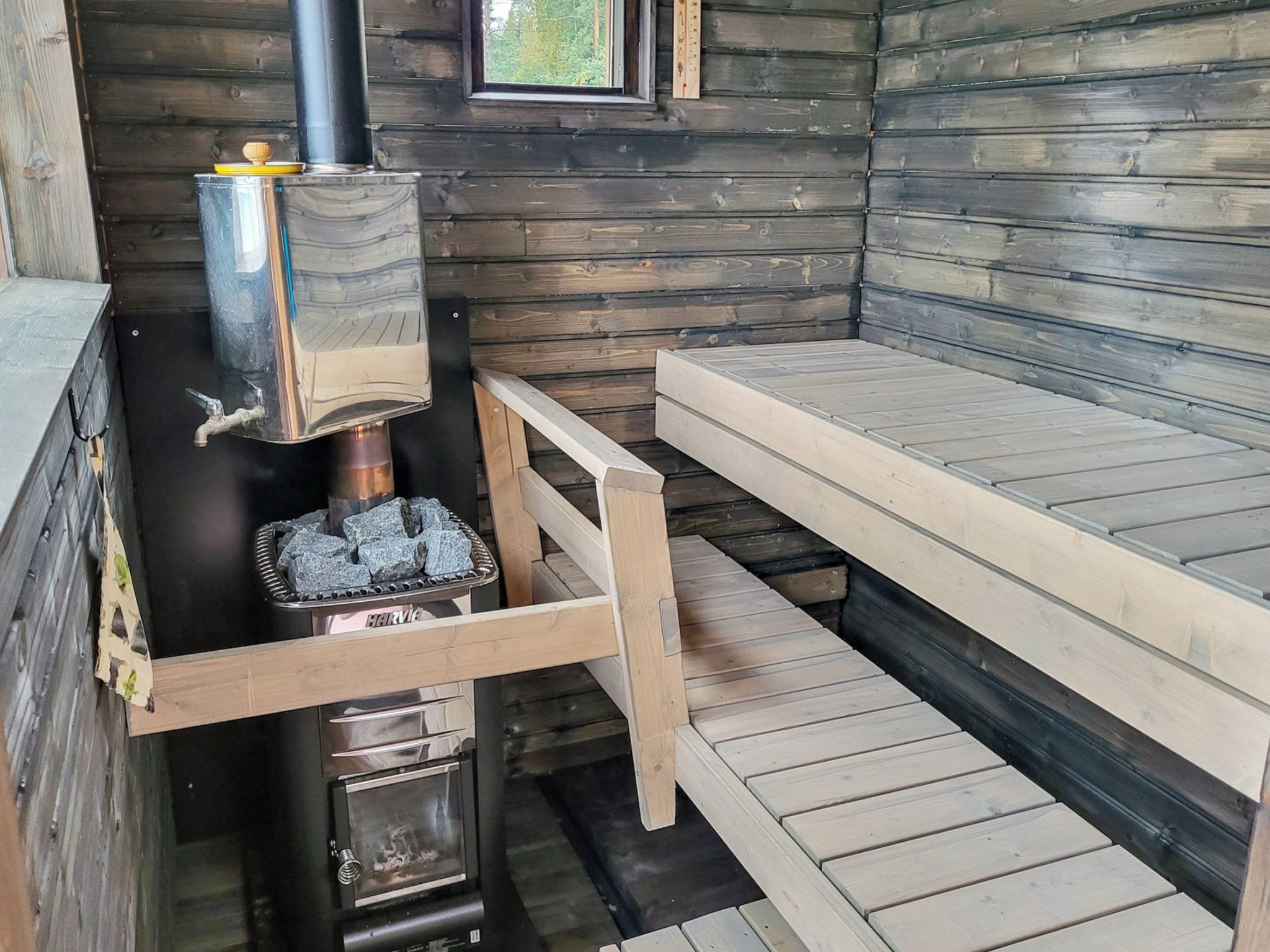 A wooden cabin interior with a wood stove, a bench, and a window.