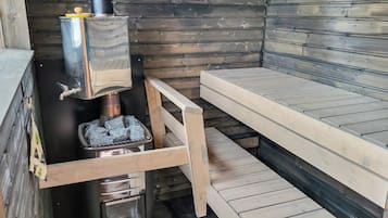 A wooden cabin interior with a wood stove, a bench, and a window.