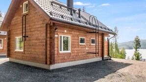 Una cabaña de madera con techo inclinado, una chimenea y un pequeño porche.