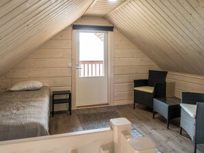 A cozy attic bedroom with a bed, a chair, a small table, and a door leading to a balcony.