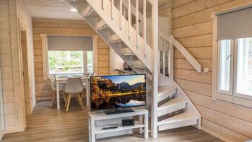 A modern interior with a wooden staircase, a dining area, and a television on a white stand.