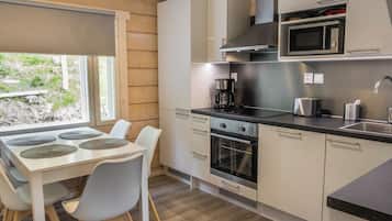 A modern kitchen with a dining area, featuring stainless steel appliances, white cabinetry, and a view of greenery outside.