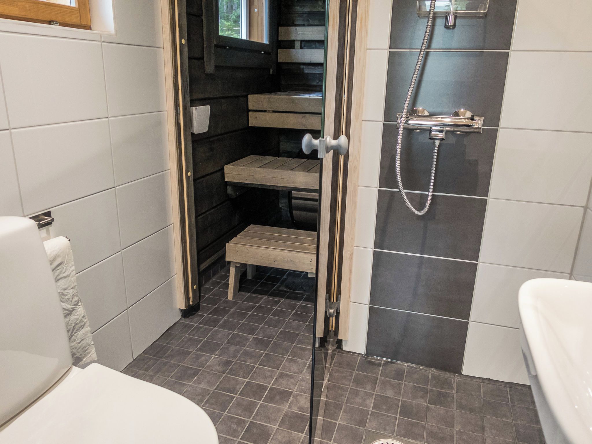 A bathroom with a shower, toilet, and a small step leading to a wooden bench.