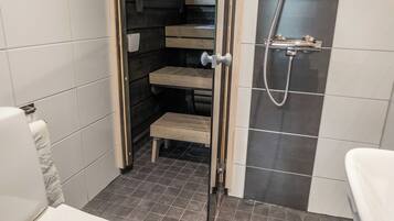 A bathroom with a shower, toilet, and a small step leading to a wooden bench.