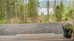A wooden deck with a potted plant, overlooking a forest and a lake.