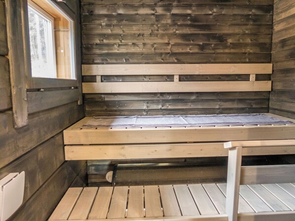 Interior de una cabaña de madera con una cama, una ventana y vistas al exterior.