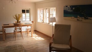 Una habitación con una mesa de comedor de madera, sillas, un jarrón con flores, una lámpara y un cuadro en la pared.