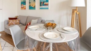 Un comedor con una mesa redonda dispuesta para cuatro personas, rodeada de sillas grises. Encima de la mesa, en la pared, hay tres cuadros enmarcados.