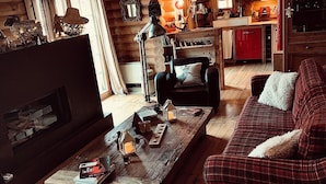 Interior acogedor de una cabaña de troncos, con una sala de estar que incluye un sofá a cuadros, una mesa de centro de madera con objetos decorativos y una chimenea.