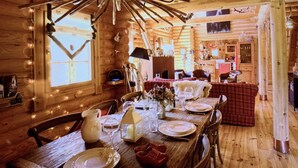 Interior de madera con una mesa de comedor para cuatro, una araña y una zona de cocina al fondo.