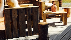 Una terraza rústica de madera con un banco y dos sillas con cojines blancos y suaves.