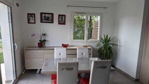 A dining area with a table and chairs, a window with a view of greenery, and a wall with framed photos. - Comfortable family home in the mountains, near lake and resorts (La Rochette)