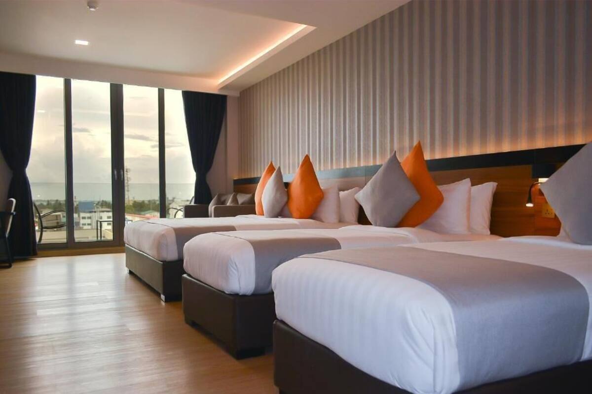 Ett hotellrum med tre sängar, ett stort fönster med gardiner och utsikt över staden.