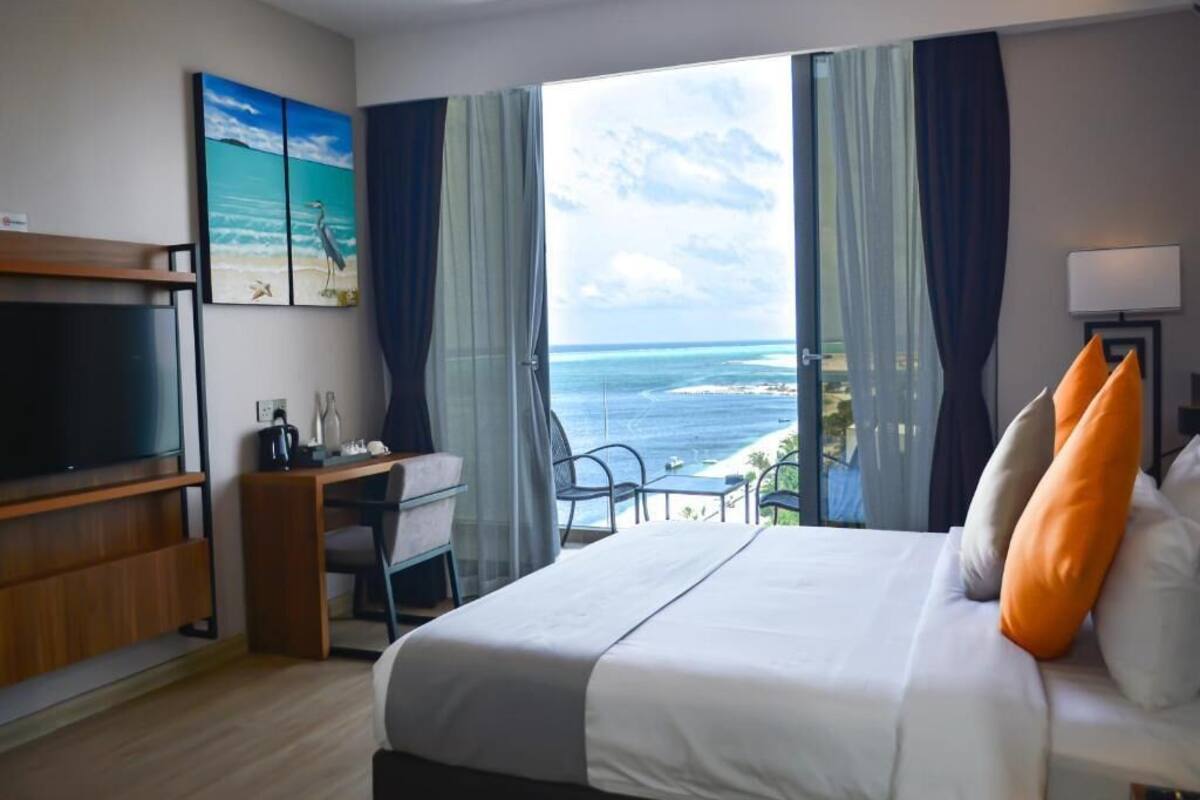 Ett hotellrum med en säng, ett skrivbord, en tv och utsikt över havet.