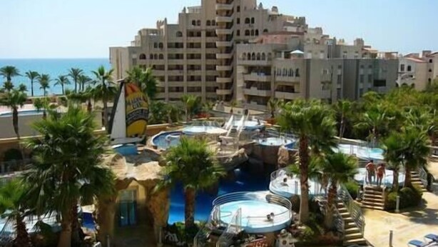 Un resort con varias piscinas, palmeras y un edificio grande al fondo.