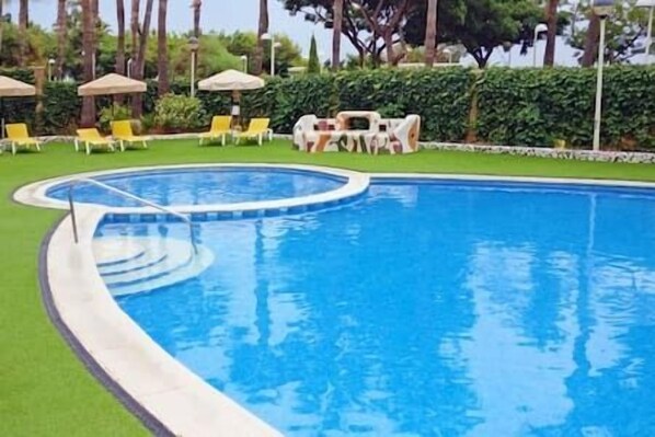 A swimming pool with a curved edge, surrounded by a well-maintained lawn and several yellow lounge chairs.