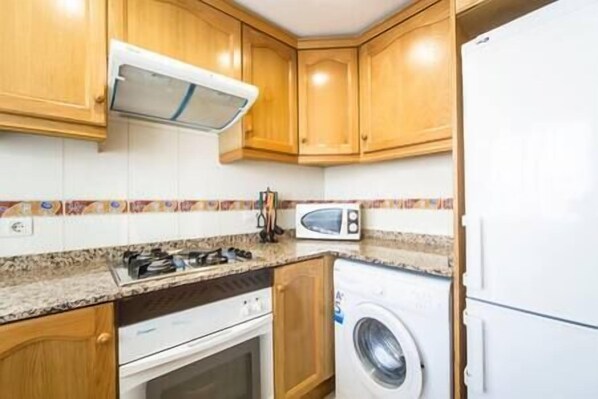A compact kitchen with wooden cabinets, a microwave, a washing machine, and a gas stove.