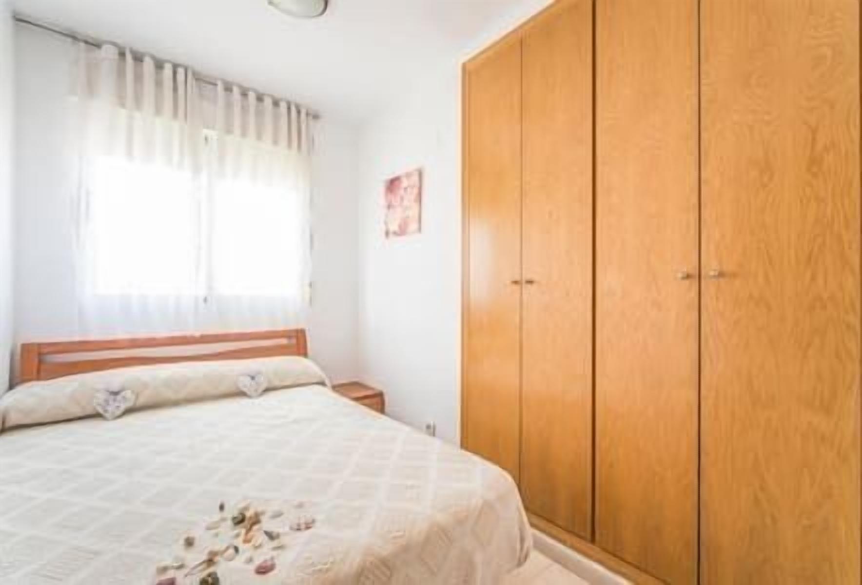 Une chambre à coucher avec un lit, une armoire en bois, une table de chevet et une fenêtre avec des rideaux.