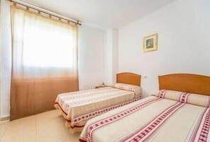 A room with two single beds, a window with curtains, and a framed picture on the wall.