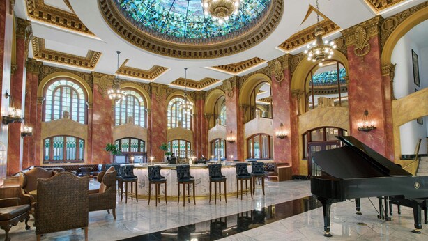 Een statig atrium met een piano, versierde zuilen en een grote glas-in-loodkoepel.