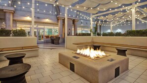 Een terras met buitenmeubilair, een vuurplaats, lichtjes en uitzicht op het interieur van het gebouw.