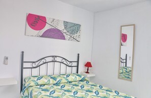 A bedroom with a bed, a nightstand, a lamp, a wall-mounted mirror, and a piece of abstract art. - Private double room with its own terrace (Conil de la Frontera)