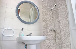 A bathroom with a round mirror, a sink with a soap dispenser, a towel ring, and a shower with a handheld showerhead.