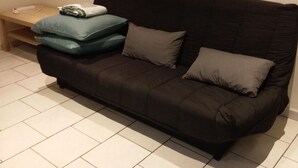 En soffa i mörk färg med två kuddar, ett litet träbord och ett vitt föremål på bordet.