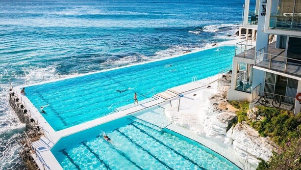 Une grande piscine extérieure située à côté d’une côte rocheuse, avec une eau d’un bleu limpide et une vue sur l’océan.