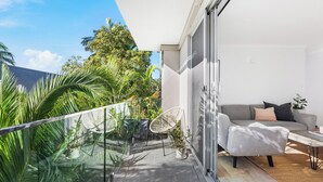 Un balcon moderne avec des garde-corps en verre, un canapé gris et une petite table, donnant sur un jardin luxuriant.