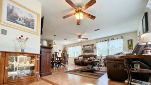 Ein geräumiges Wohnzimmer mit Holzdielen, Kamin, Essbereich und Deckenventilator.